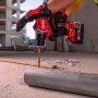 Milwaukee M18 BLPDRC-422C slagboremaskine, en kompakt og kraftfuld kulfri løsning med 145 mm længde til nem adgang i snævre områder. Billedet er et miljøbillede, hvor man kan se bygninger i baggrunden.