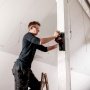 En person bruger en trådløs Metabo excentersliber til at fjerne maling fra en stolpe