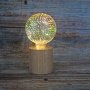 Haarhr & Co LED bordlampe m/træfod, pære m/fyrværkerieffekt. Billedet er et miljøbillede med træ baggrund.